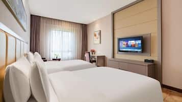 A hotel room with two beds, a TV, a desk, and a window with curtains.