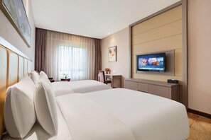 Ein Hotelzimmer mit zwei Betten, einem Fernseher, einem Schreibtisch und einem Fenster mit Vorhängen.
