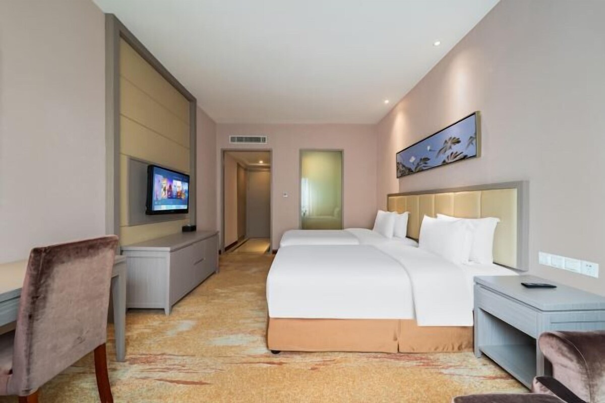 Quarto de hotel com uma cama, uma escrivaninha, uma televisão e um quadro na parede.