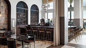 A modern bar area with a high bar counter, multiple stools, and a large window with decorative iron grilles.