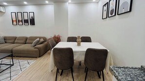 Una sala de estar moderna con un sofá color beige, una mesa de comedor con cuatro sillas y un jarrón decorativo.