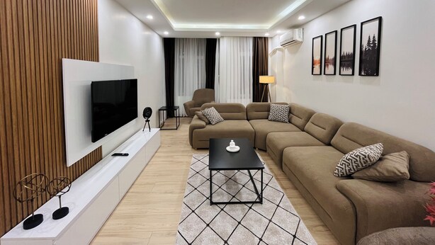 Una sala de estar moderna con un sofá seccional, un televisor de pantalla plana, una mesa de centro y una alfombra estampada.