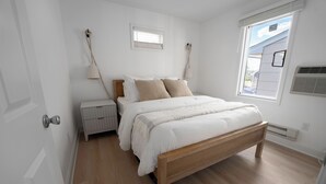 Une chambre à coucher avec un lit en bois, une literie blanche, une table de chevet, une lampe et une fenêtre avec des stores.