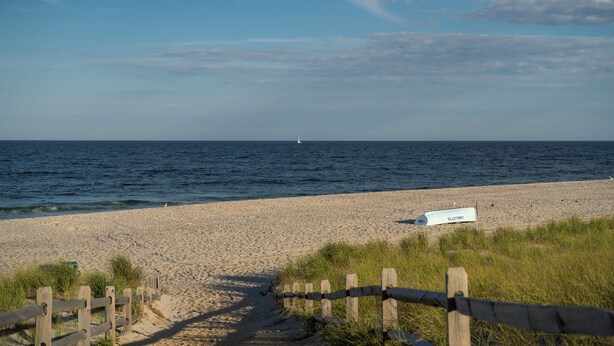 Une plage de sable bordée d’une clôture en bois qui mène à l’eau, une tour de surveillance pour les sauveteurs et un ciel dégagé.
