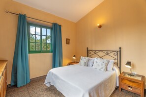 Un dormitori amb un llit, cortines, una finestra, una làmpada de nit i una làmpada penjada a la paret.