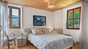 Een slaapkamer met een bed, een stoel, een nachtkastje, een lamp en een raam met uitzicht op bergen.