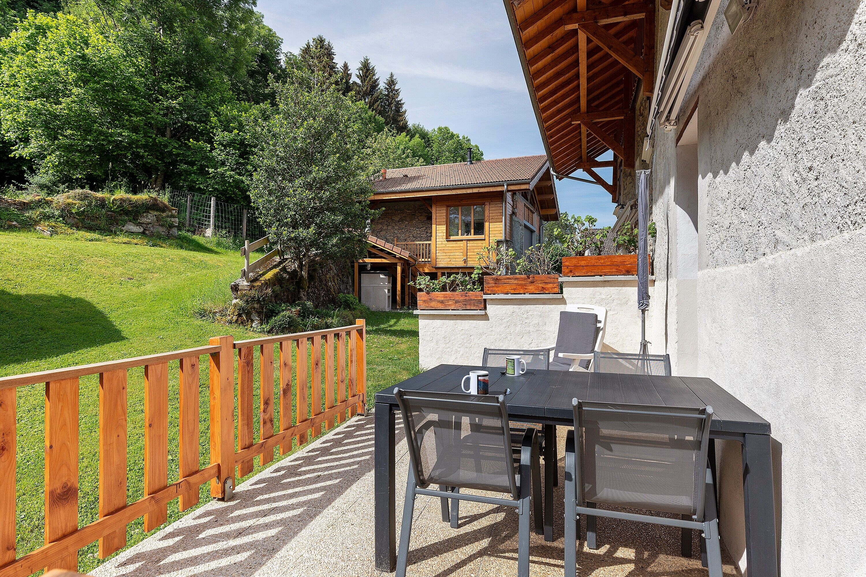 A patio with a table and chairs, a wooden fence, and a house with a stone facade and a sloped roof.