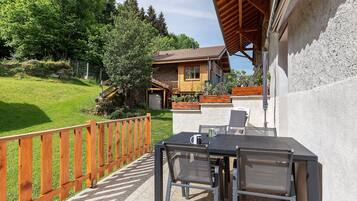 A patio with a table and chairs, a wooden fence, and a house with a stone facade and a sloped roof.