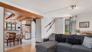 Een moderne woonkamer met een grijze modulaire bank, houten vloeren en een eethoek met een geruit tafelkleed.