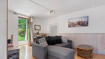 A modern living room with a grey sectional sofa, a round wooden coffee table, and a large window offering a view of greenery.