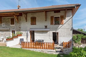 A rustic stone building with wooden shutters, a balcony with a wooden railing, and outdoor seating.