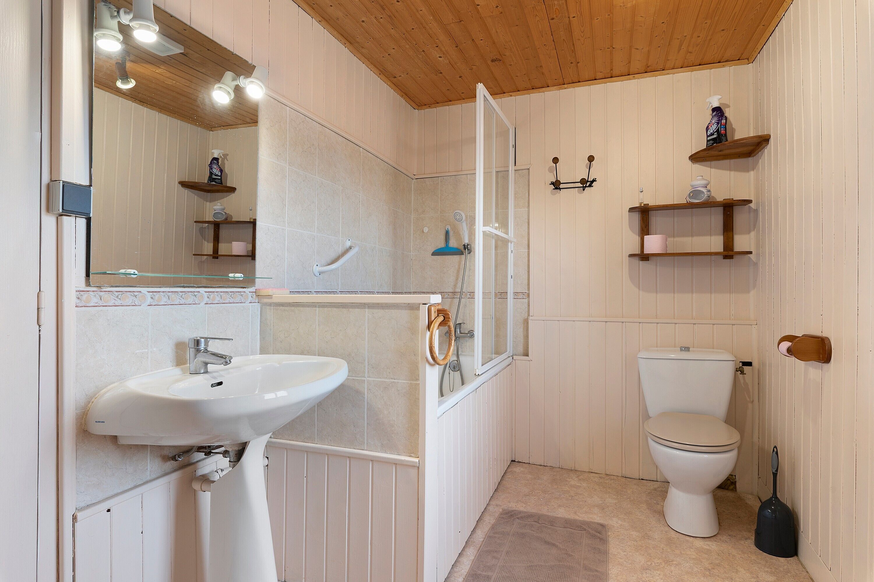 Ein Badezimmer mit einem weißen Waschbecken, einer Toilette, einer Dusche und Holzregalen mit Pflegeprodukten.