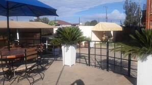 An outdoor patio area with tables and chairs, covered by umbrellas, and surrounded by a metal fence. - Hotel Luna Nakuru (Nakuru)