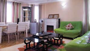 A modern living room with a green sofa, a fireplace, a dining area with chairs and a table, and a large mirror. - Hotel Luna Nakuru (Nakuru)