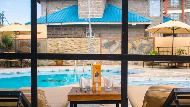 A poolside area with lounge chairs, a table with a bottle of sunscreen, and a view of a building with a blue roof. - Hotel Luna Nakuru (Nakuru)