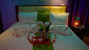 A hotel room with a neatly made bed, a bottle of champagne, and rose petals arranged on the bed. - Hotel Luna Nakuru (Nakuru)