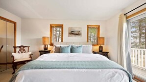 Une chambre avec un grand lit, deux lampes de chevet, une chaise et une fenêtre donnant sur les arbres.