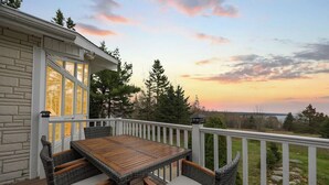 Une terrasse avec une table et des chaises, offrant une vue sur un paysage naturel avec des arbres et un coucher de soleil.