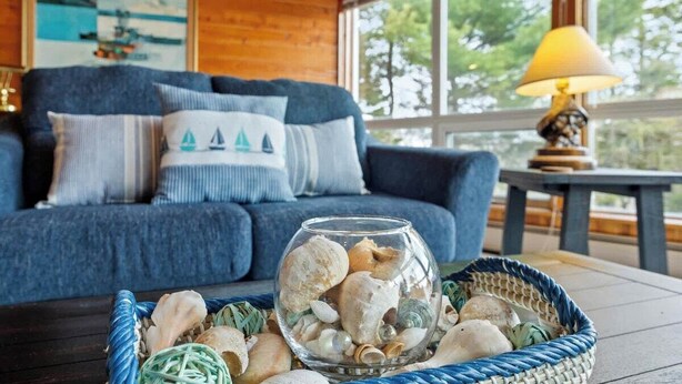 Une pièce chaleureuse avec un canapé bleu, un bol en verre rempli de coquillages et une lampe sur une table.