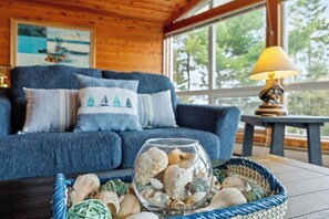 A cozy room with a blue sofa, a glass bowl with seashells, and a lamp on a table. - Spectacular Ocean View, AC, Firepit, Deck! (Lamoine)