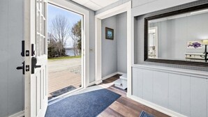 A hallway with a door leading to a view of a body of water, a framed picture on the wall, and a mirror reflecting part of the room. - New! Lakeview at Branch Lake (Ellsworth)