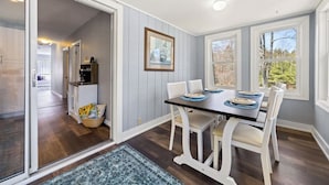 A dining area with a table set for four, white chairs, a dark table, and a view through large windows. - New! Lakeview at Branch Lake (Ellsworth)