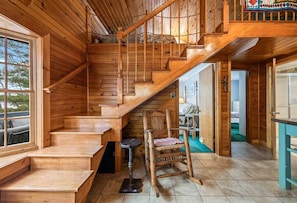 A wooden staircase leading to a loft area, a rustic chair, and a small table.