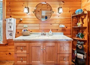 Une salle de bain rustique, aménagée dans une cabane en bois, avec un lavabo, un miroir, un porte-serviettes et une décoration sur le thème de l’ours.