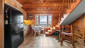 A wooden cabin interior with a kitchen, dining area, and a staircase leading to a loft. - Moose Lodge on the Lake (Ellsworth)