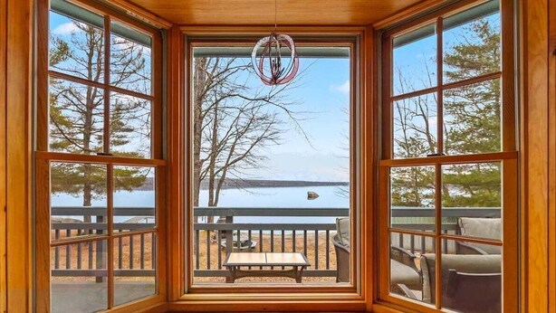 A room with large windows, a wooden ceiling, and a view of a lake and deck furniture. - Moose Lodge on the Lake (Ellsworth)
