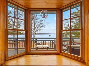 A room with large windows, a wooden ceiling, and a view of a lake and deck furniture. - Moose Lodge on the Lake (Ellsworth)