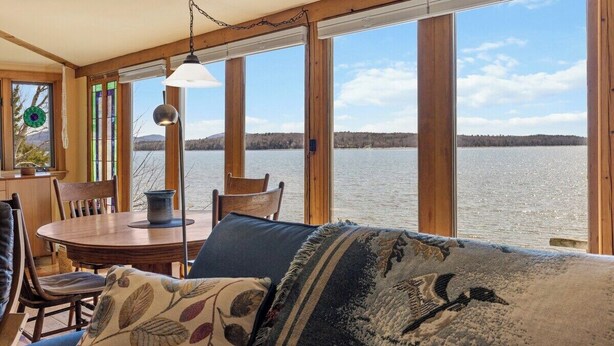 A room with a wooden interior, large windows, a round table, and chairs. - Berry Cove Cottage-Oceanfront! (Lamoine)