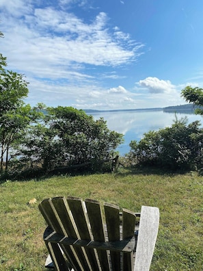 A wooden chair facing a calm lake with trees in the background.