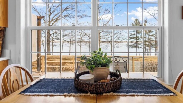 A dining area with a table, chairs, a potted plant, and a view through large windows. - Cove & Cottage at Newbury Neck (Surry)