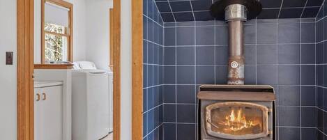 A room with a wood-burning stove, a washing machine, and a mirror on the wall.