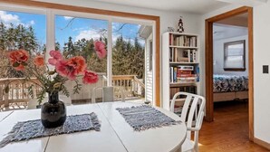 Zona pranzo con tavolo, sedie, un vaso con fiori, una libreria e vista sull'esterno.