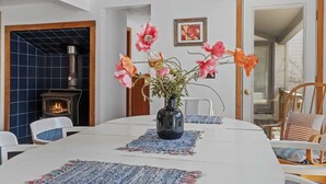 Un'area pranzo con un tavolo bianco, un vaso con fiori, una stufa a legna e una parete rivestita di piastrelle blu.