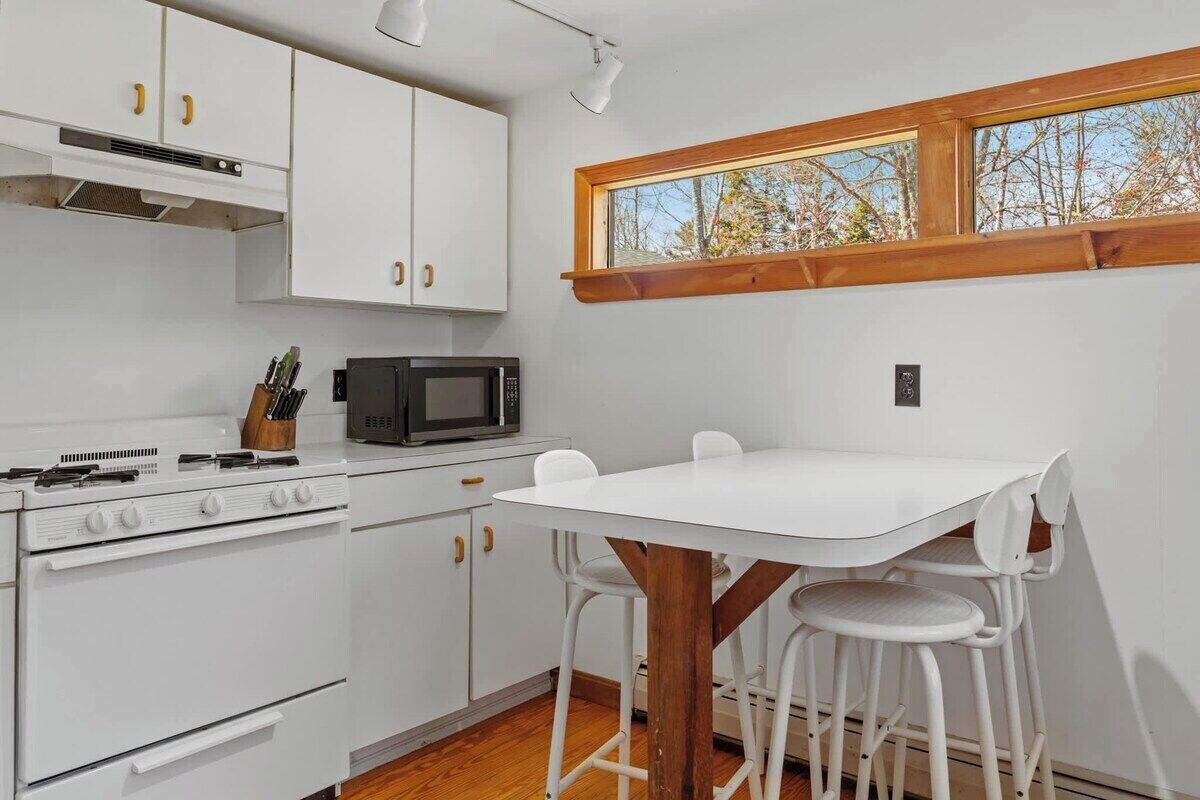 Une cuisine de taille réduite avec des meubles blancs, une cuisinière, un four à micro-ondes et une table à manger avec des chaises.