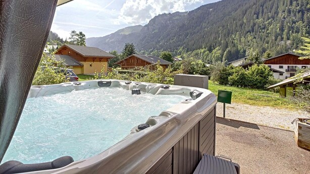 Un bain à remous avec vue sur les montagnes, des chalets en bois et un ciel dégagé.