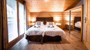 Une chambre aux murs lambrissés, avec deux lits, des lampes de chevet et un grand miroir.