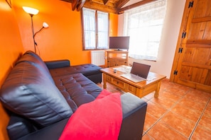 A living room with a sofa, a wooden coffee table, a television, and a window with curtains.