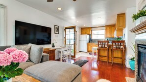 A modern living room with a sofa, a flat-screen TV, and a dining area with wooden chairs and a table. - Steps to Ocean: Manhattan Beach Gem w/ Deck! (Manhattan Beach)