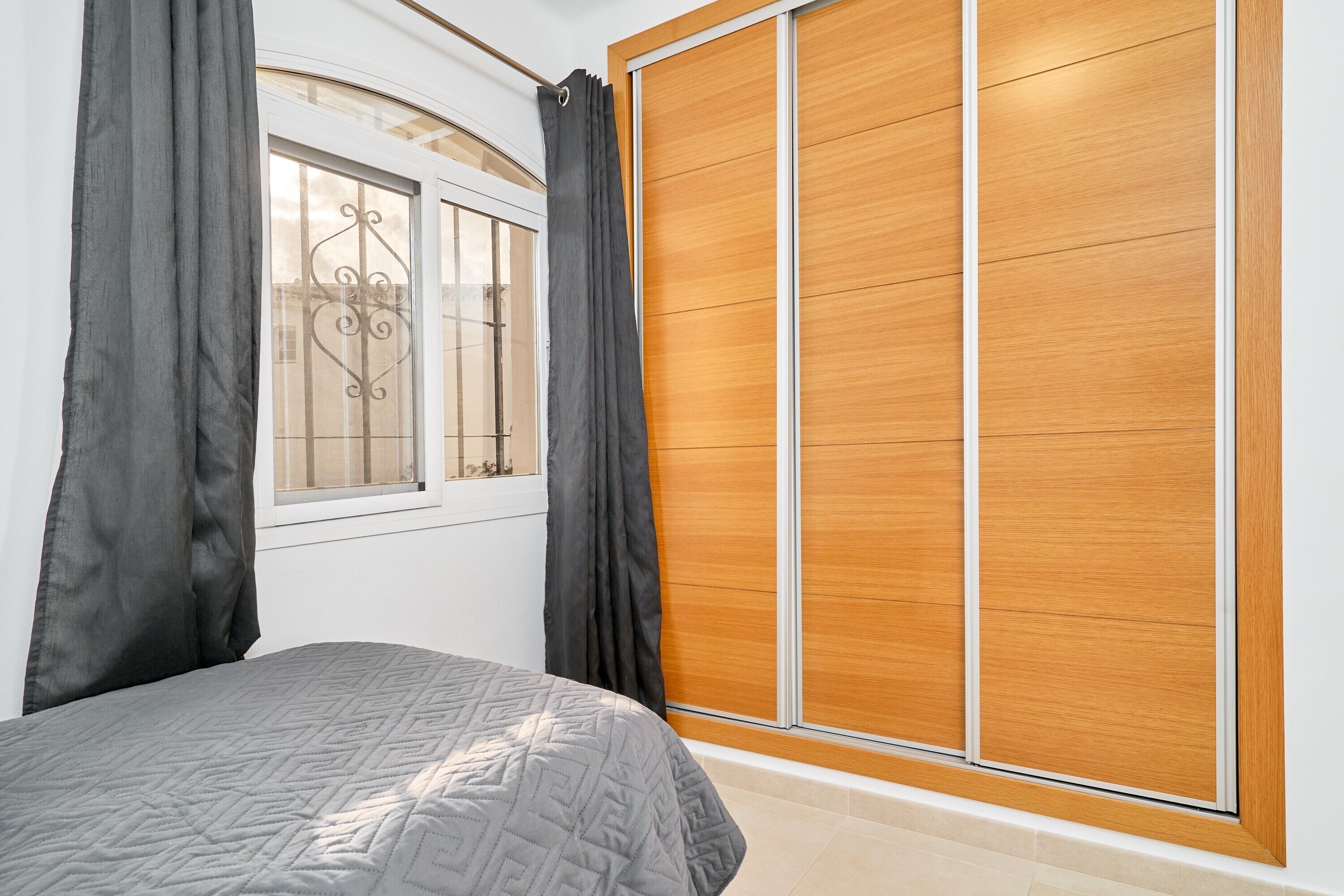 A bedroom with a bed, a window with curtains, and a wooden wardrobe.
