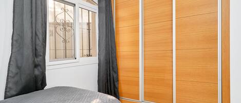 A bedroom with a bed, a window with curtains, and a wooden wardrobe.