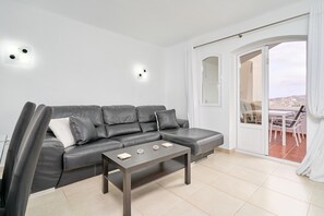 Un salon moderne avec un canapé gris, une table basse et une porte-fenêtre coulissante donnant sur un espace extérieur.