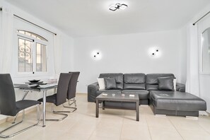 Un salon moderne avec un canapé d’angle, une table basse en verre et un coin repas comprenant une table et des chaises.
