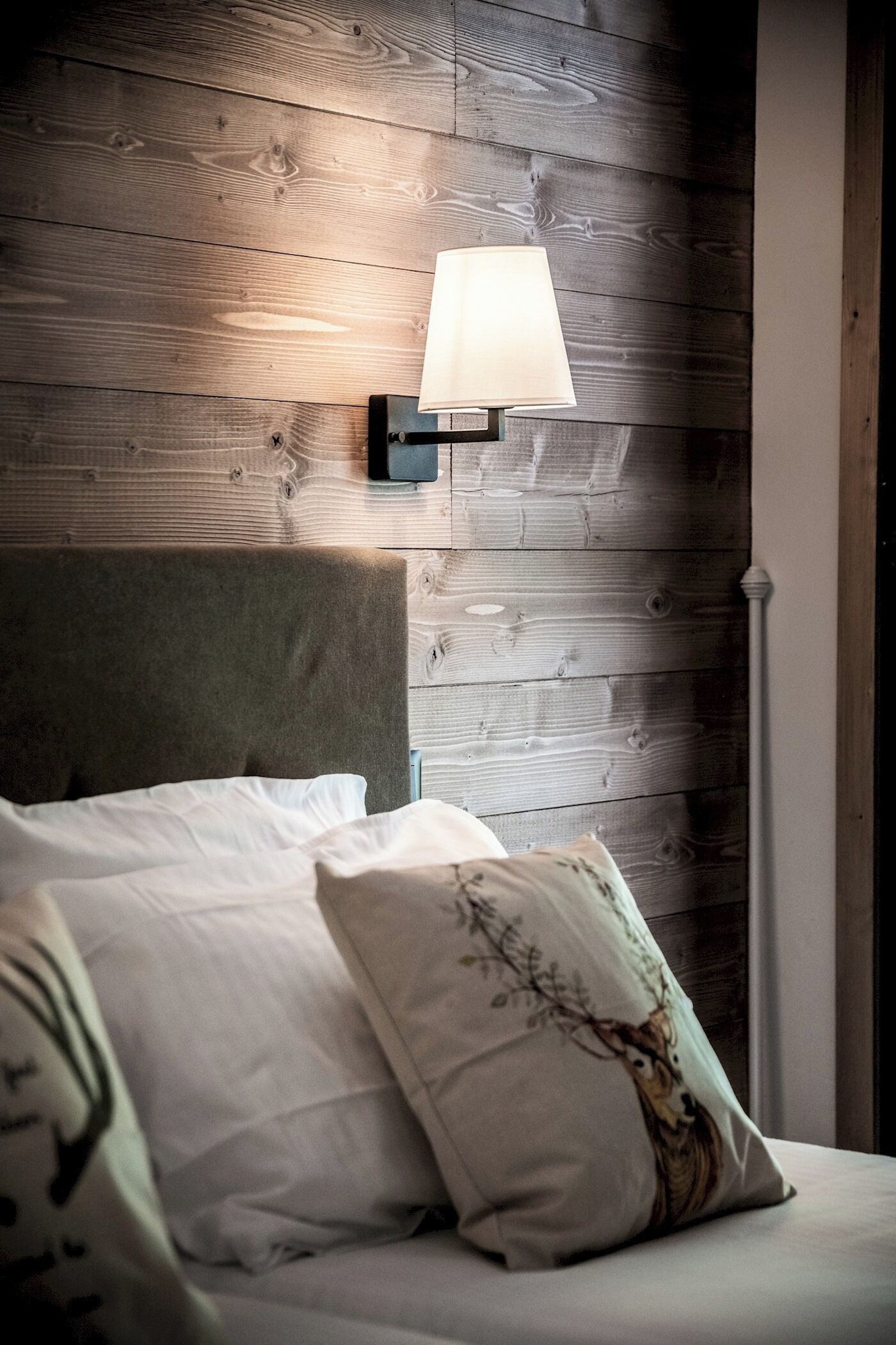 Et soveværelse med sengegavl i træ, en sengebordlampe og seng med hvide sengetøj og dekorative puder.