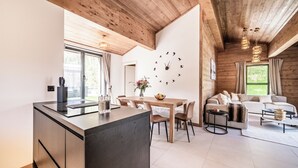 Una cocina moderna con techo de madera, un comedor con mesa y sillas de madera, y una sala de estar con sofá y mesa de centro.
