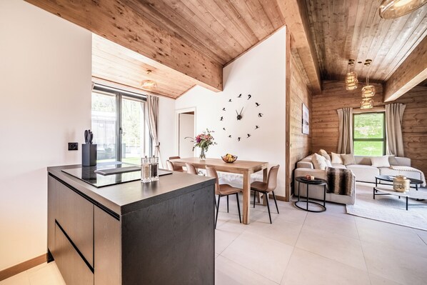 A modern kitchen with a wooden ceiling, a dining area with a wooden table and chairs, and a living room with a sofa and coffee table.
