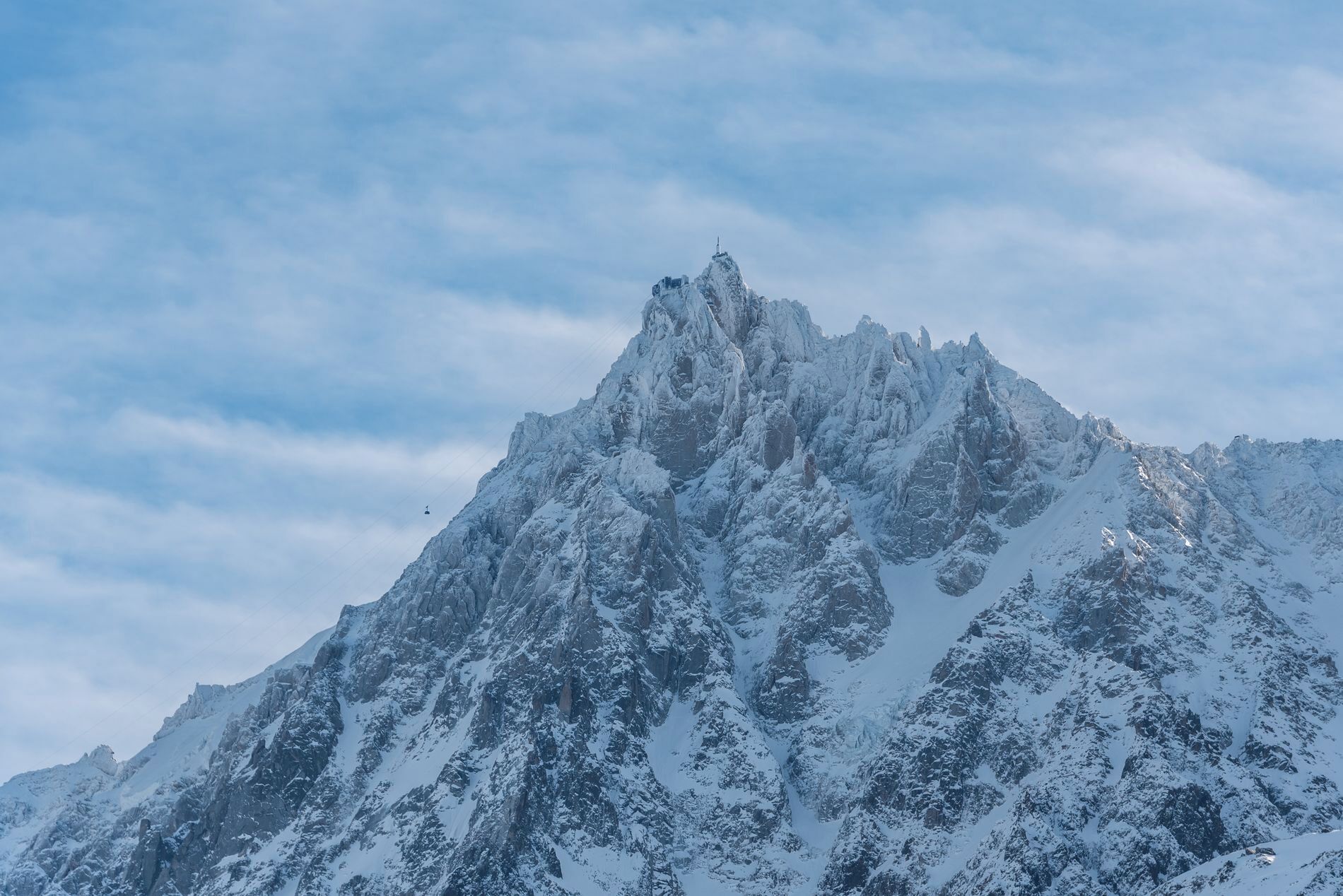 Ein mit Schnee bedeckter Berggipfel mit zerklüftetem Gelände und blauem Himmel.